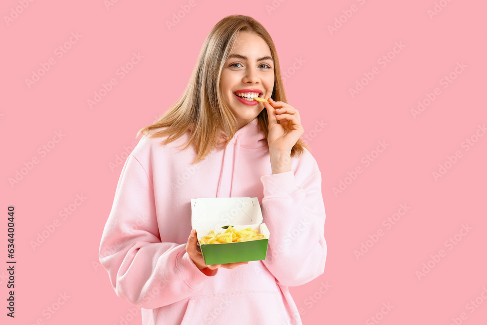 Beautiful young woman eating french fries on pink background