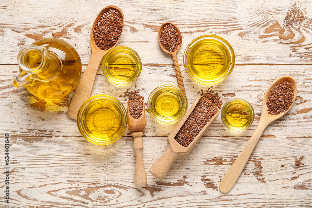 Glass bowls of flax oil and spoons with seeds on white wooden background