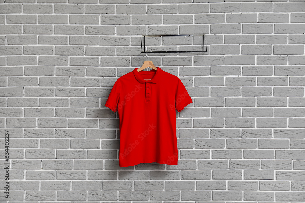 Stylish red t-shirt hanging on grey brick wall