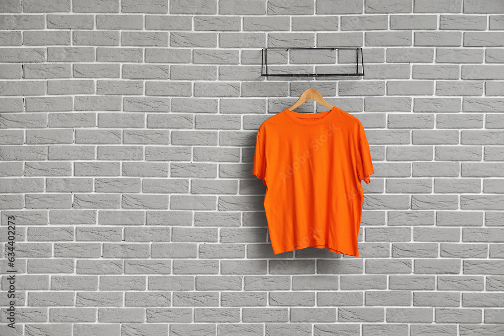 Stylish orange t-shirt hanging on grey brick wall