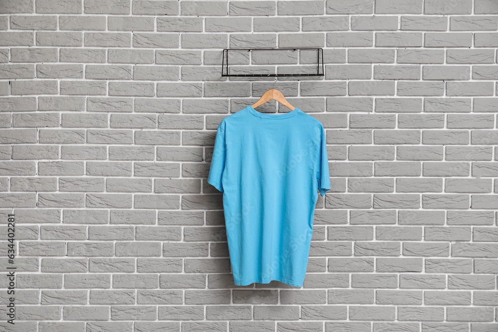 Stylish blue t-shirt hanging on grey brick wall