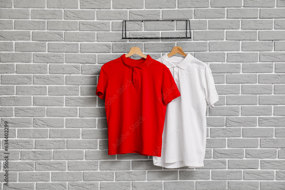 Stylish t-shirts hanging on grey brick wall