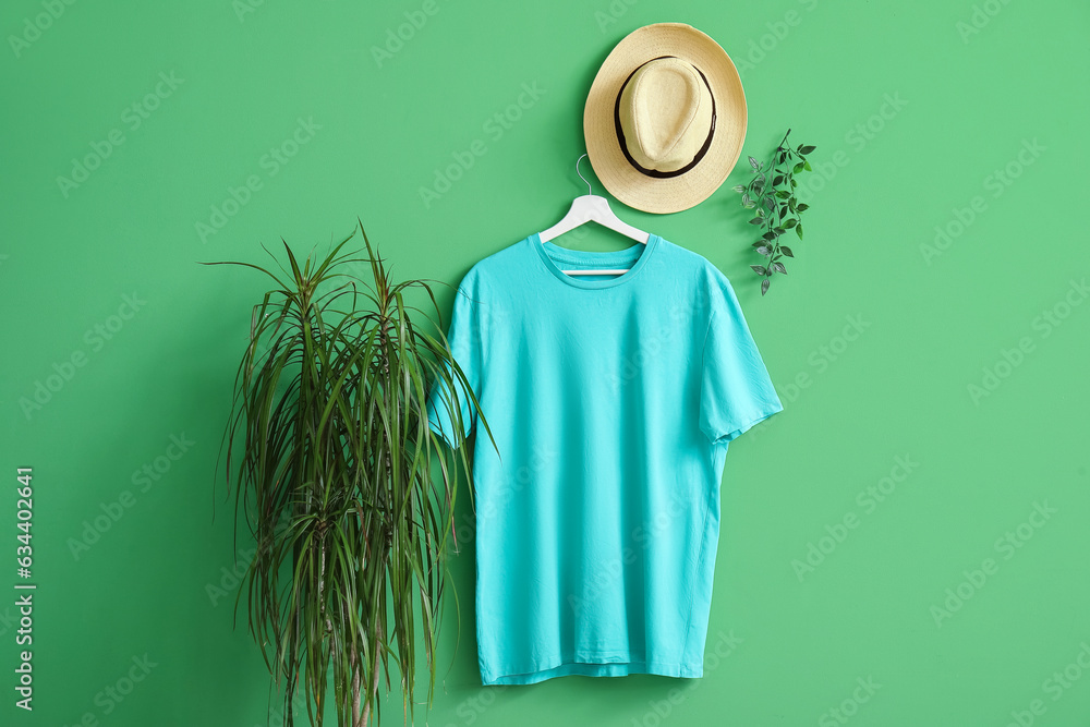 Stylish blue t-shirt and hat hanging on green background