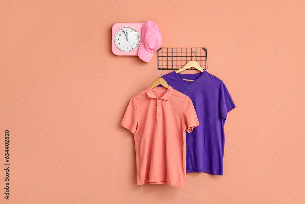 Stylish t-shirts and cap hanging on pink background