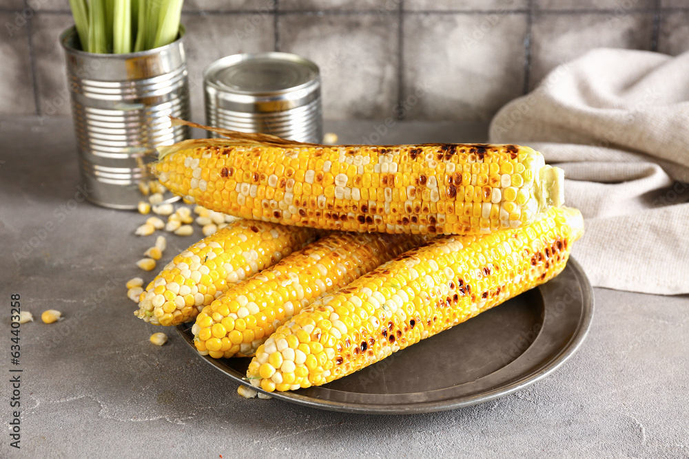 Plate with tasty grilled corn cobs and seeds on grey table