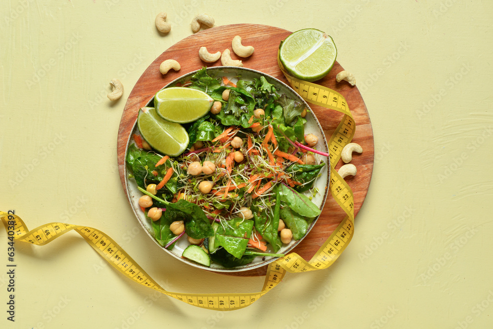 Plate with fresh salad and measure tape on yellow background. Diet concept