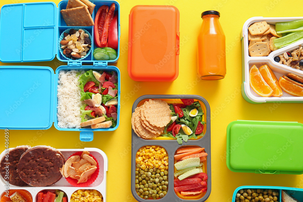 Many lunchboxes with different delicious food and bottle of juice on yellow background