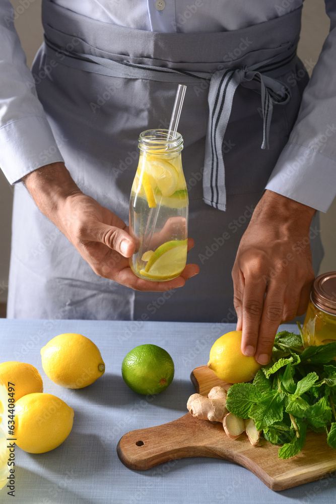 Man holding bottle of tasty lemonade with lime on grey background