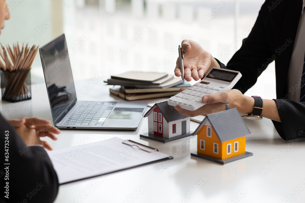 Businessman, real estate agent holding a calculator, presenting a price quote to a client for a hous