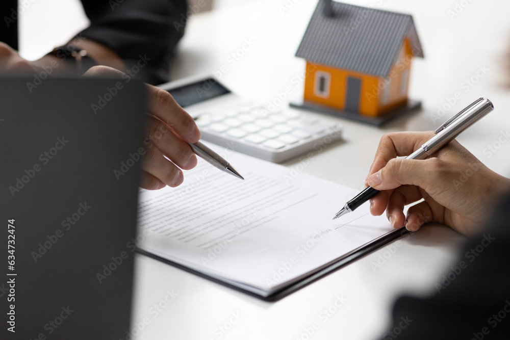 Real estate agent holding pen pointing at contract document for client to sign home purchase agreeme