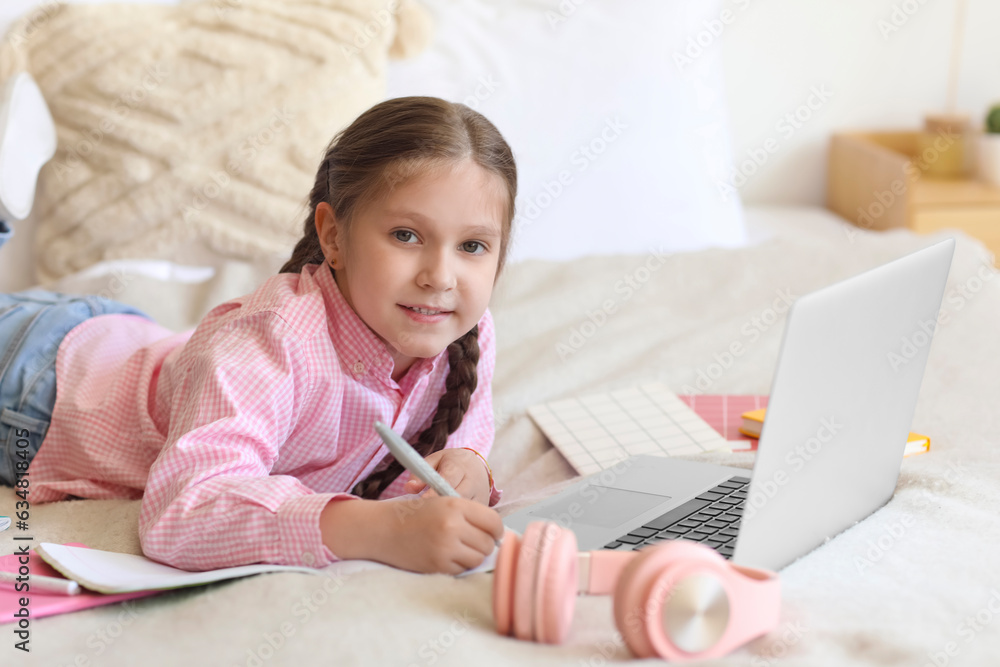 Little girl with laptop studying computer sciences online in bedroom