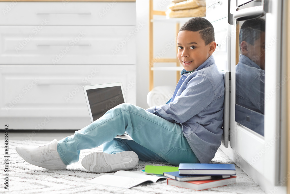 Little African-American boy with laptop studying computer sciences online in kitchen