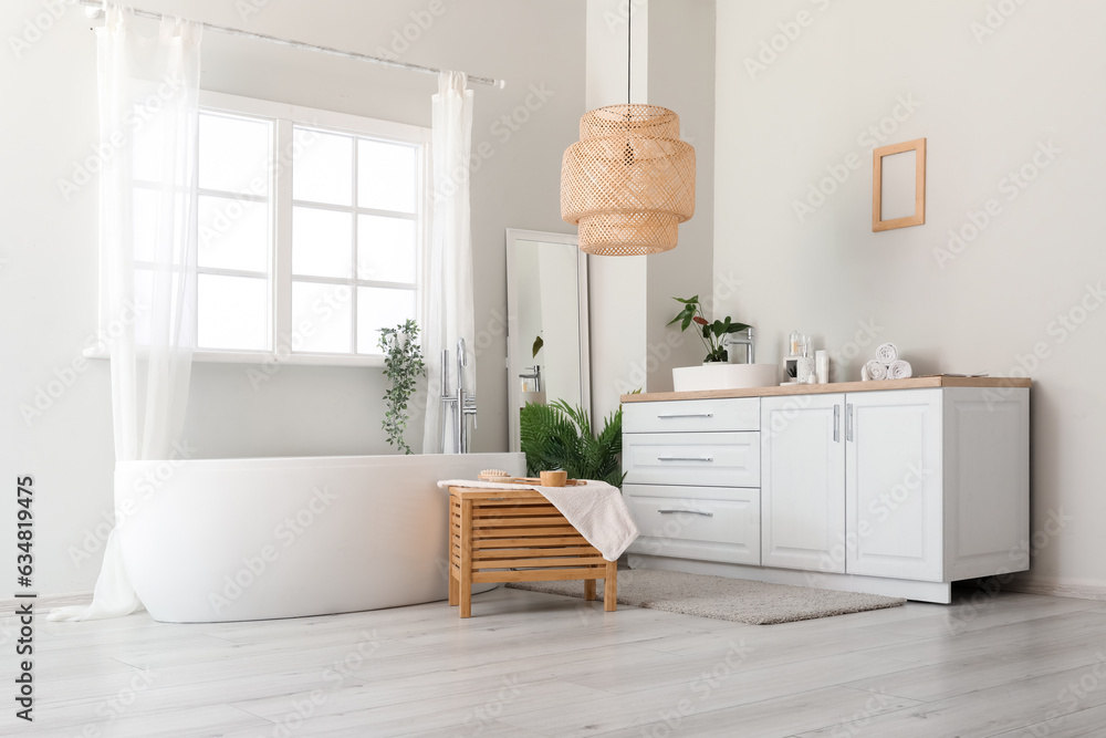 Interior of light bathroom with sink bowl on white counters, mirror and bathtub