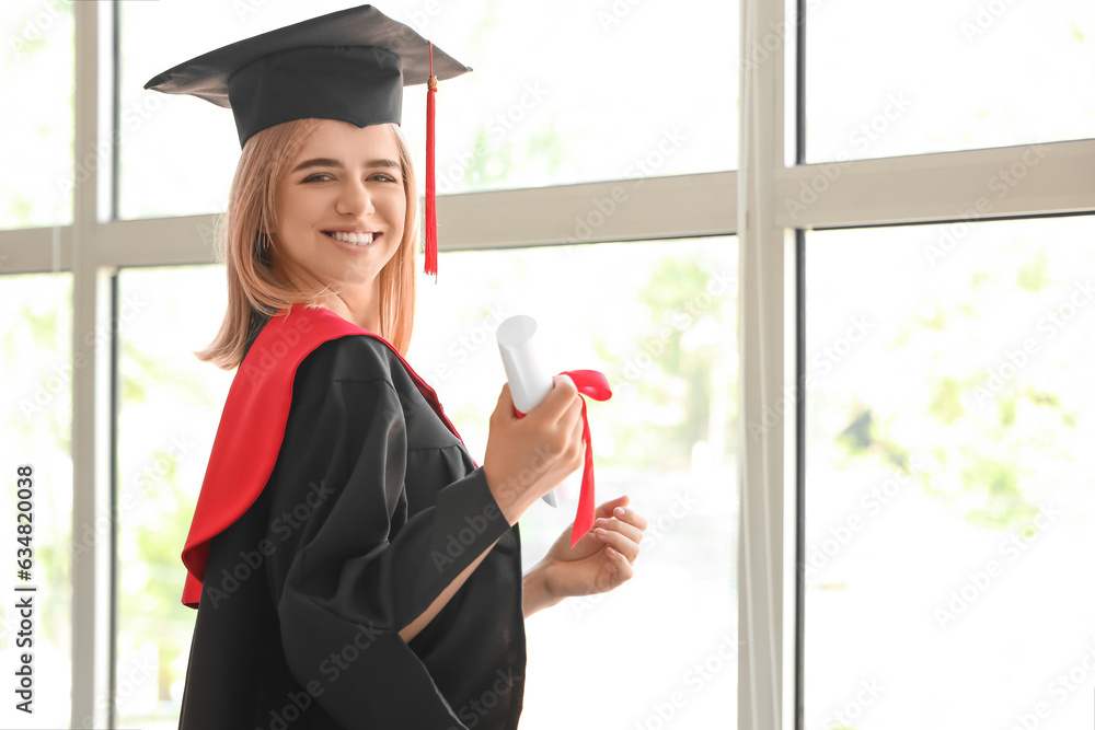 Female graduate student with diploma near window in room