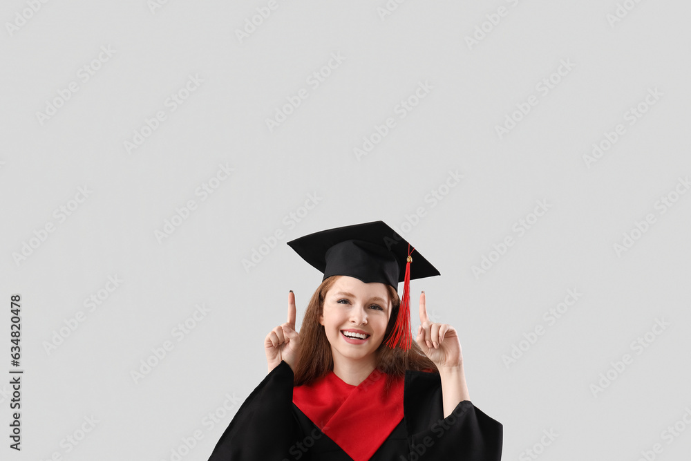 Female graduate student pointing at something on grey background