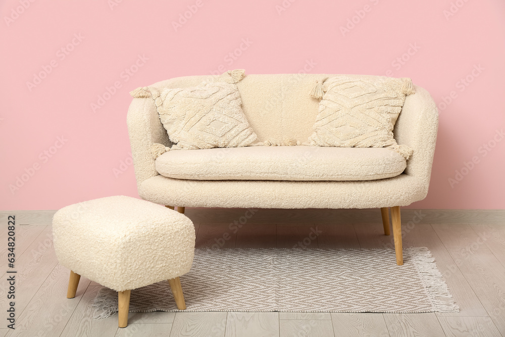 Cozy white sofa with pillows and ottoman near pink wall