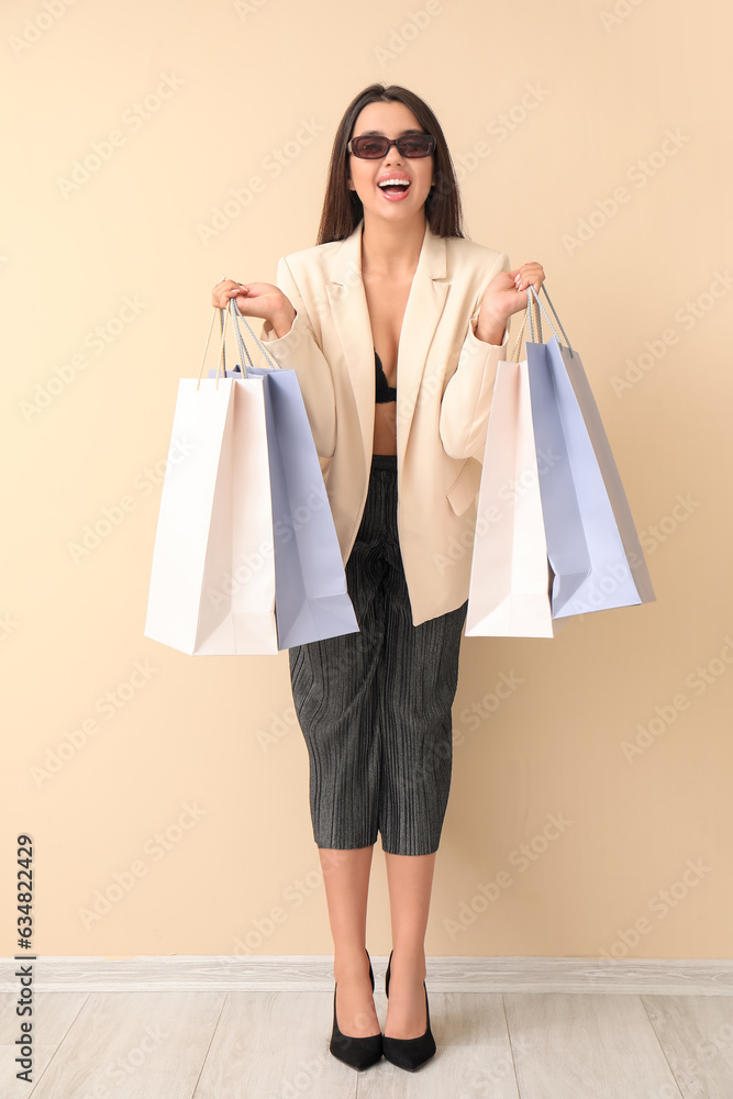 Happy beautiful young woman with shopping bags near beige wall