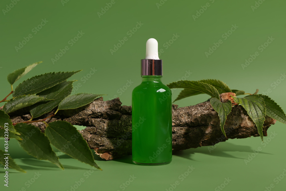 Bottle of cosmetic oil with tree bark and leaves on green background