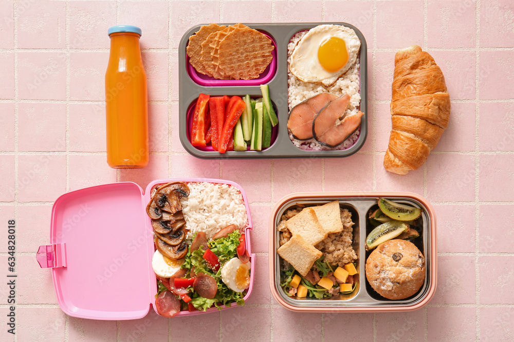 Lunchboxes with different delicious food and bottle of juice on pink tile background