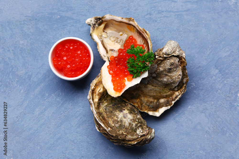 Tasty oysters with red caviar on blue background