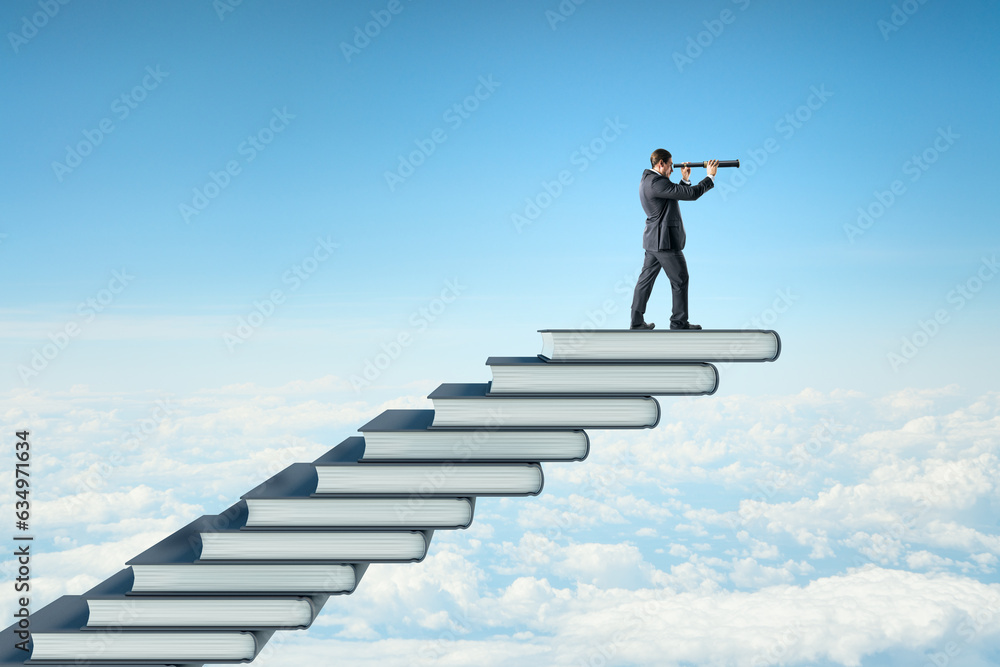 Side view of young businessman with telescope on top of book steps on bright blue sky with clouds ba