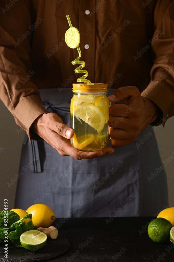 Man holding mason jar of tasty lemonade with mint and lime on black table