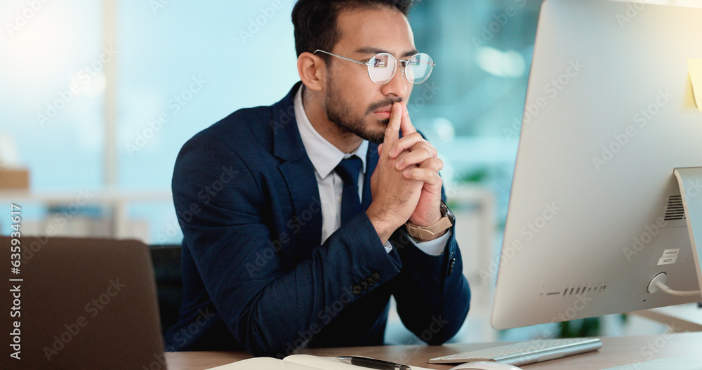 Thinking IT manager working on a desktop computer and laptop in a modern office. Information Technol