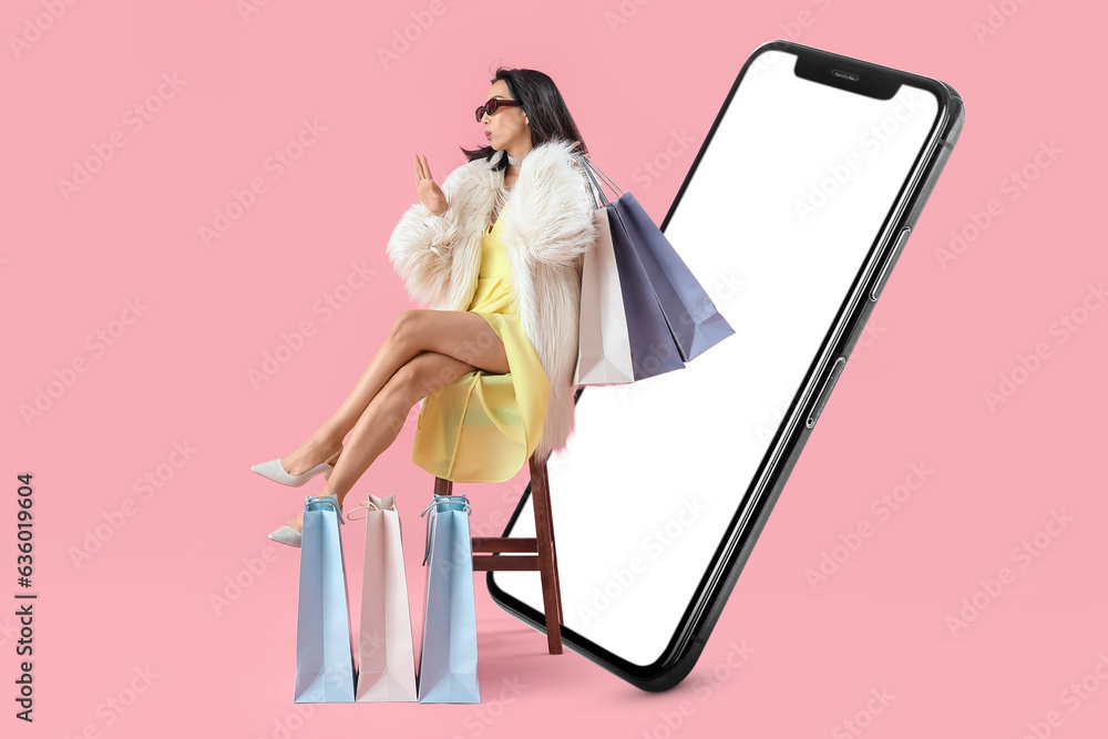 Stylish Asian woman with shopping bags and big mobile phone on pink background