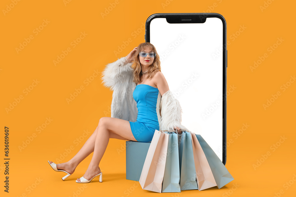 Stylish woman with shopping bags and big mobile phone on yellow background