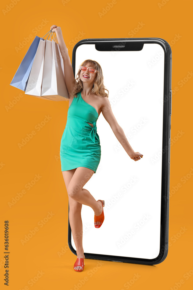 Stylish woman with shopping bags and big mobile phone on yellow background