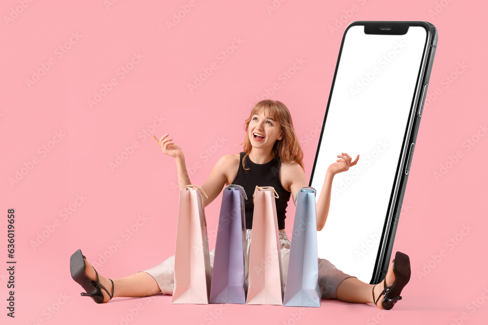 Sitting young woman with shopping bags and big mobile phone on pink background