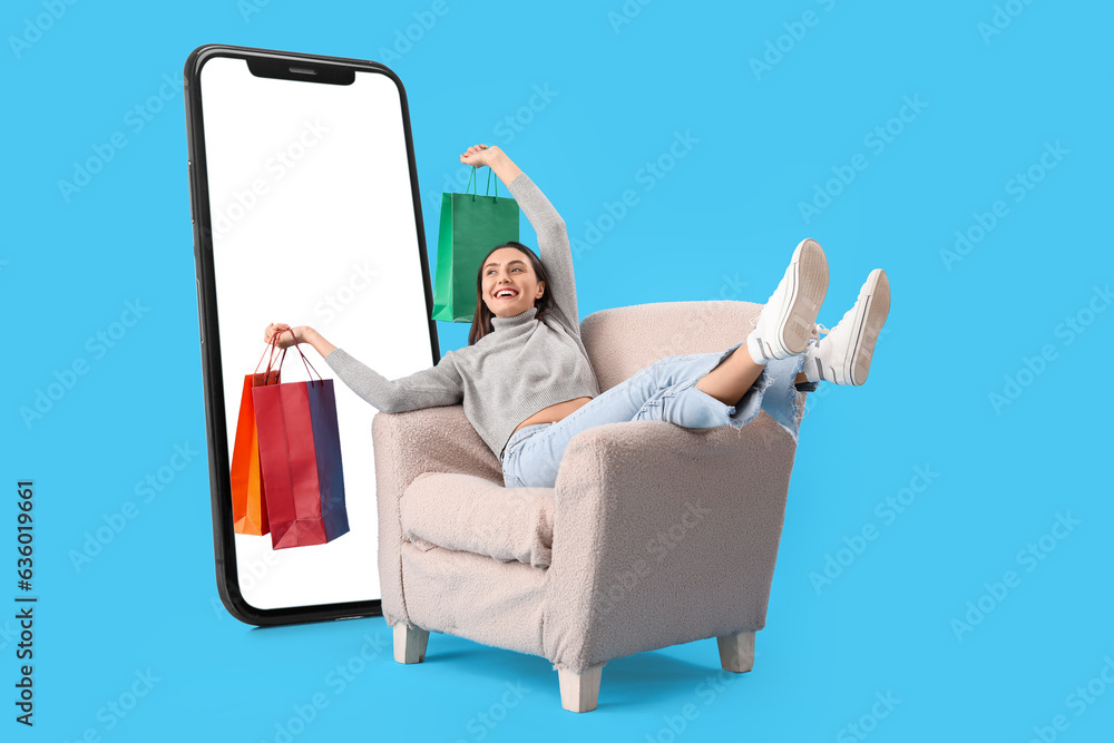 Happy woman with shopping bags sitting in armchair near big mobile phone on light blue background