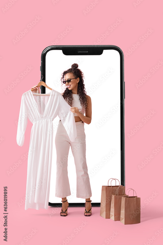 Stylish woman with new dress and shopping bags near big mobile phone on pink background