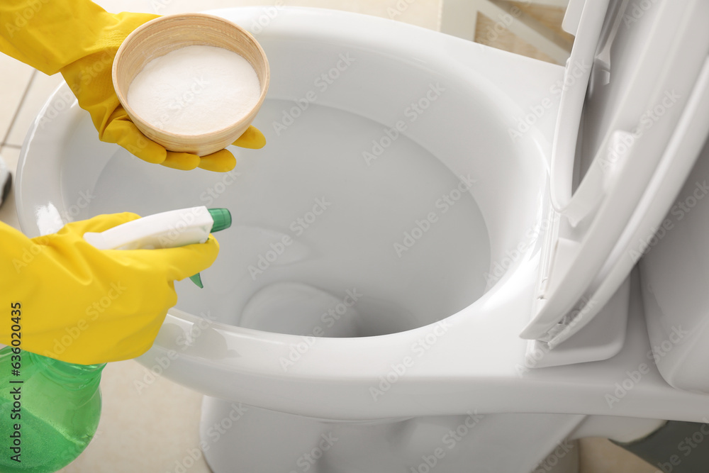 Woman in rubber gloves cleaning toilet bowl with baking soda and sprayer, closeup