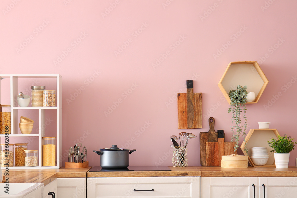 Electric stove with cooking pot and utensils on kitchen counter near pink wall