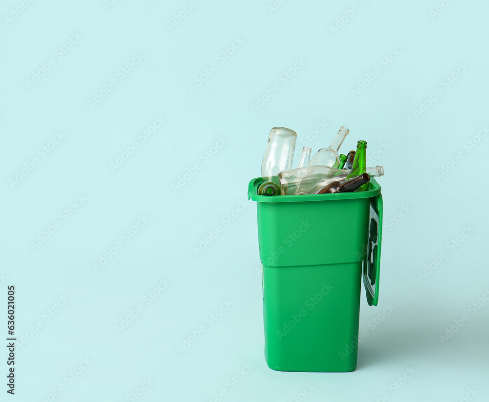 Container for garbage with glass bottles on light blue background. Recycling concept