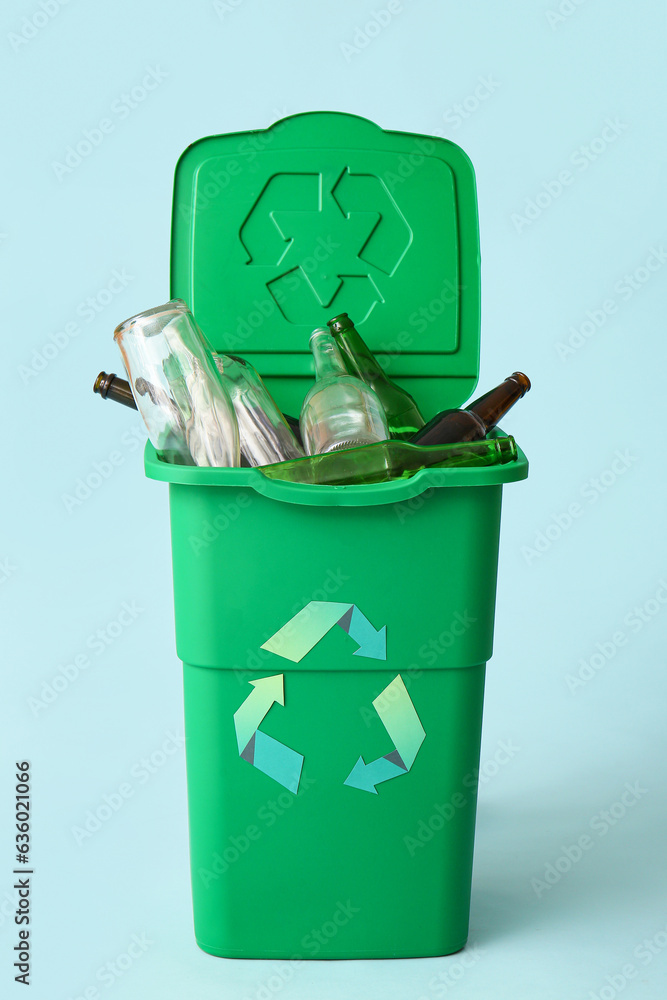 Container for garbage with glass bottles on light blue background. Recycling concept