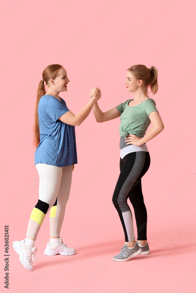 Portrait of sporty young women holding hands on pink background