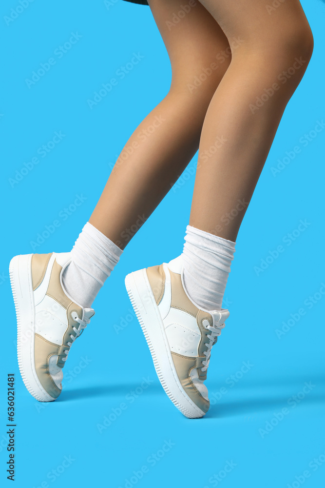 Female legs in stylish sneakers on color background, closeup