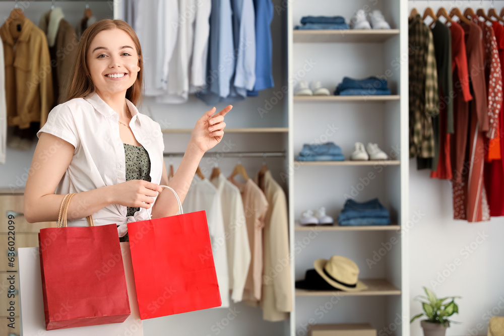 Young woman with shopping bags pointing at something in boutique