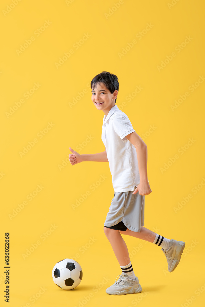 Little boy playing with soccer ball on yellow background