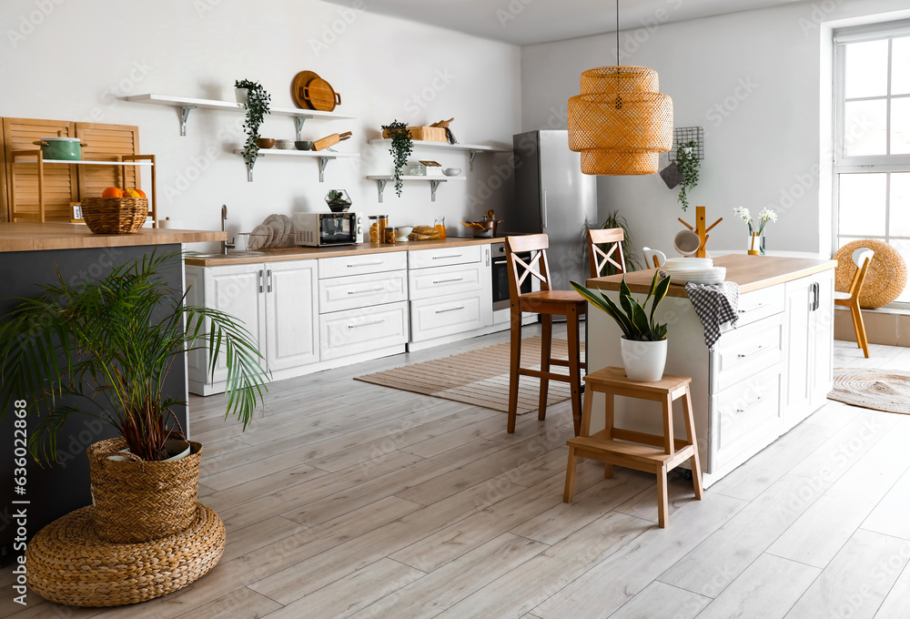 Interior of light kitchen with stylish fridge, counters, shelves and houseplants