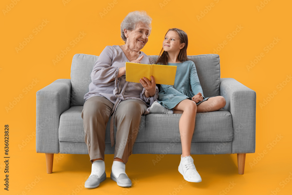 Little girl with her grandmother reading book on yellow background