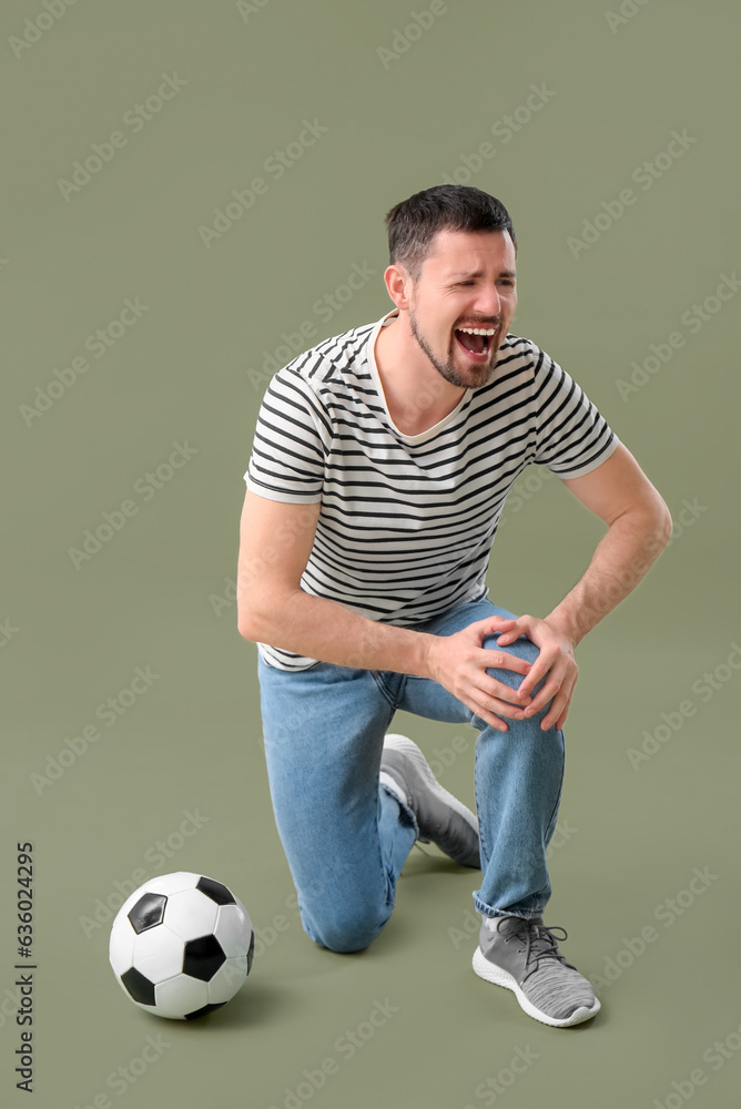 Screaming man with injured leg and soccer ball on color background