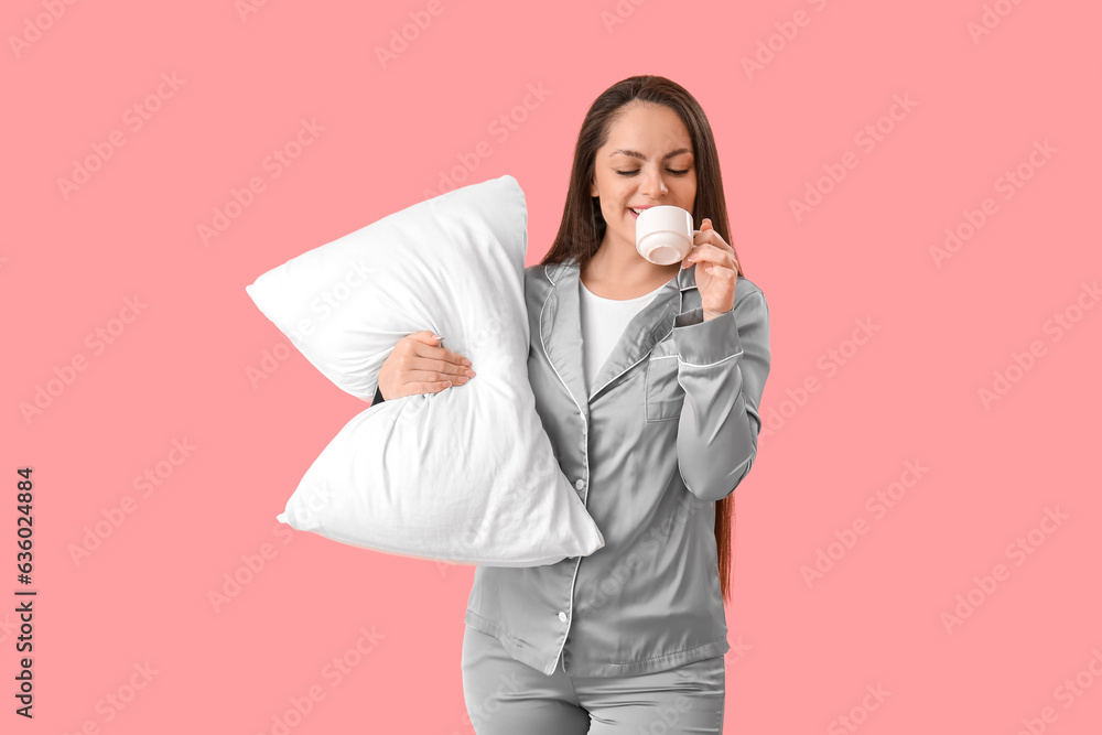 Pretty young woman with pillow drinking coffee on pink background