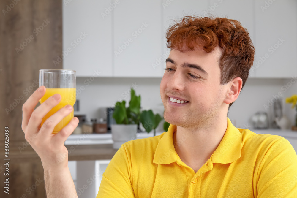 Young man with glass of orange juice in kitchen, closeup