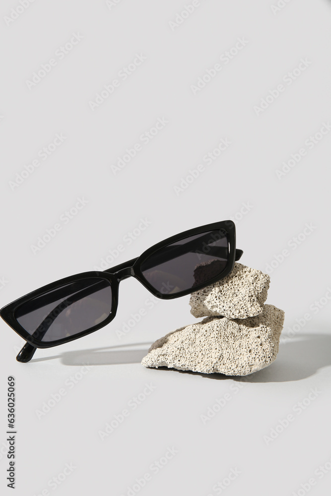 Stones with stylish sunglasses on grey background