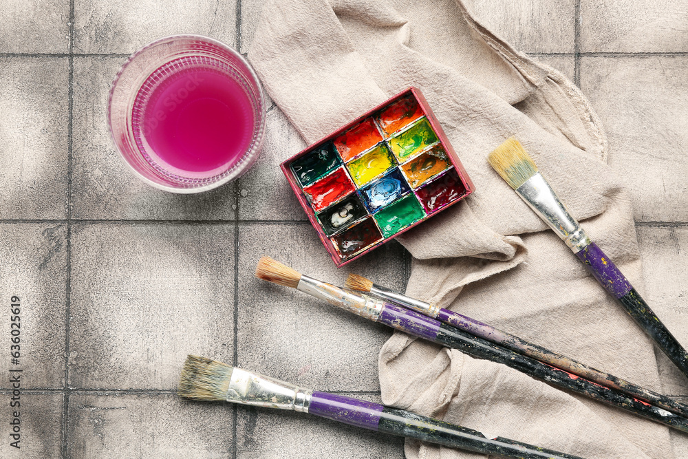 Artists paints with brushes, cloth and glass on grey tile background