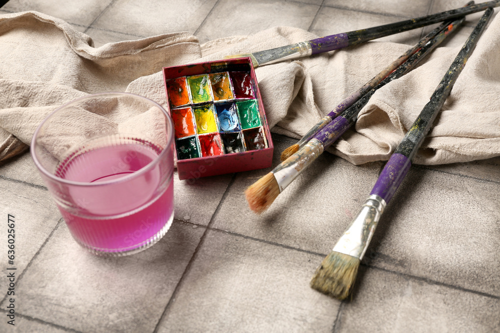 Artists paints with brushes, cloth and glass on grey tile background