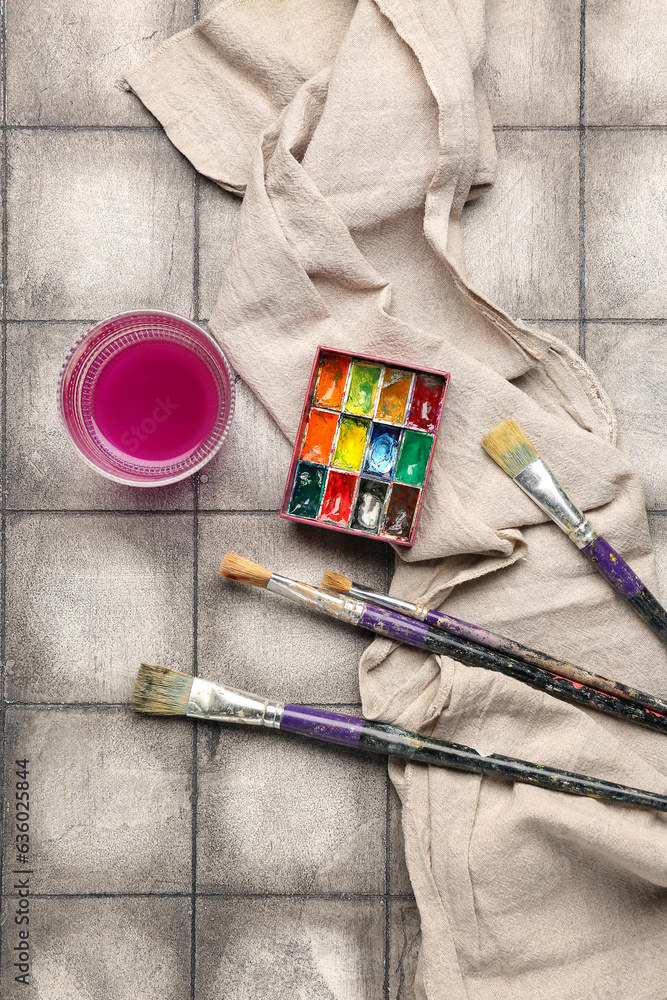 Artists paints with brushes, cloth and glass on grey tile background